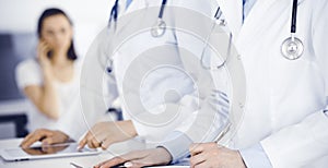 Unknown woman-doctors at work with patient at the background. Female physicians filling up medical documents or