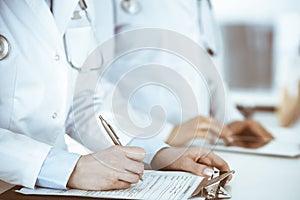 Unknown woman-doctors at work with patient at the background. Female physicians filling up medical documents or