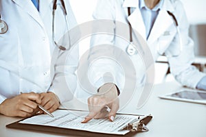 Unknown woman-doctors at work with patient at the background. Female physicians filling up medical documents or