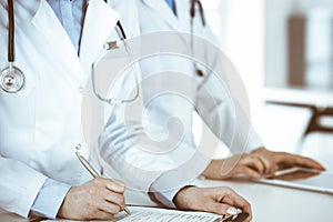 Unknown woman-doctors at work with patient at the background. Female physicians filling up medical documents or