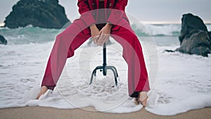 Unknown woman sitting chair on beach sand wearing red stylish suit close up.