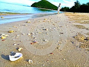 Unknown woman walking on seashell sandbeach with sea and hill background