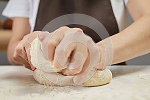 Unknown woman wearing brown apron kneading dough on table sprinkled with flour preparing for baking bread