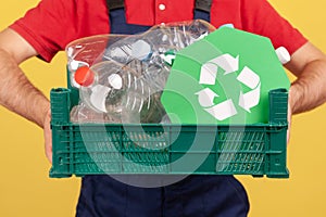 Unknown worker man holding box with plastic bottles ans green recycling symbol, ecological problems.
