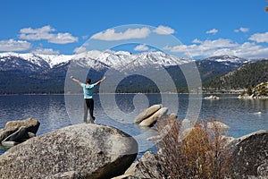 Unknown young man celebrates while standing on a boulder in scenic Lake Tahoe.
