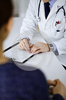 Unknown young woman patient discuss the results of her medical tests with a doctor, while sitting at the desk in a