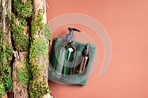 Unlabelled cosmetic bottle on brown background, natural moss over branches, bark. Skin care, organic body treatment, spa