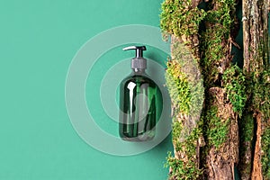 Unlabelled cosmetic bottle on green background, natural moss over branches, bark. Skin care, organic body treatment, spa