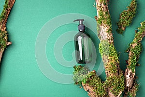 Unlabelled cosmetic bottle on green background, natural moss over branches, bark. Skin care, organic body treatment, spa