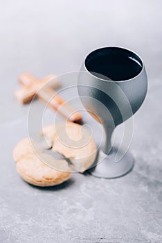 Unleavened bread, chalice of wine, wooden cross on grey background. Christian communion for reminder of Jesus sacrifice. Easter