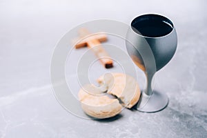 Unleavened bread, chalice of wine, wooden cross on grey background. Christian communion for reminder of Jesus sacrifice. Easter