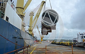 Unloading a large  shipping vessel bearing the name `Jumbo shipping` enters dock carrying  pressure storage vessels.