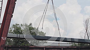 Unloading of the profile pipe by a gantry crane from a freight car, loads metal in a warehouse, a large gantry crane