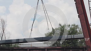 Unloading of the profile pipe by a gantry crane from a freight car, loads metal in a warehouse, a large gantry crane