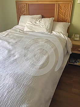 Unmade bed in a hotel room with two white pillows and a white duvet,blanket
