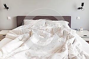 Unmade messy bed with white bedsheet in the morning.