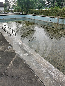 unmaintained outdoor swimming pool with algae floating on the water surface.