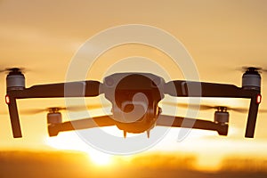 Unmanned quadcopter in flight with a digital camera at sunset. Drone silhouette at sunset