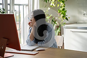 Unmotivated lazy girl sits at desk with computer and looks out window unwillingness to do work