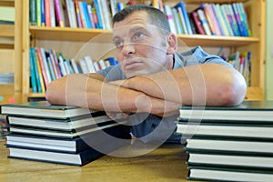 unmotivated man leaning on two stacks books in library
