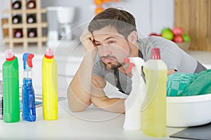 unmotivated man surrounded by cleaning products