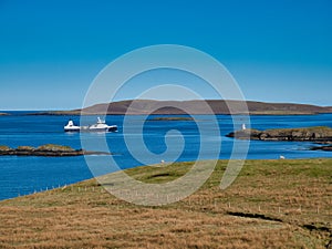 An unnamed blue and white boat sails on calm water toward Lerwick in Shetland, Scotland, UK. Taken on a calm, sunny day