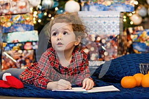 Unny pensive little girl writing letter to santa. kid making a wish, gift, present on new year eve.