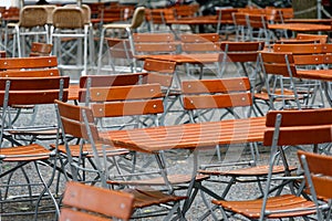 Unoccupied chairs and tables in a garden restaurant with table legs and chair legs made of iron and wooden tops