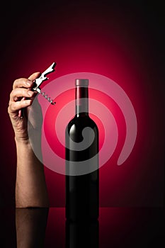 Unopened bottle of red wine and hands with corkscrew photo