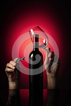 Unopened bottle of red wine and hands with corkscrew and wine glass