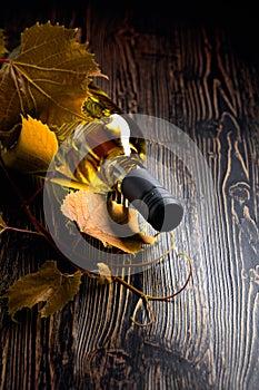 An unopened bottle of white wine and grapevine on an old wooden table