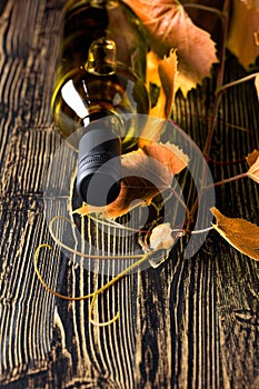 An unopened bottle of white wine and grapevine on an old wooden table