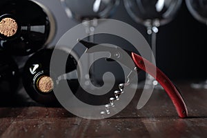 Unopened bottles of red wine, corkscrew, and empty wine glasses on an old wooden table