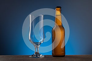 Unopened beer bottle and empty beer glass on a wooden table blue background