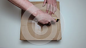Unpacking the parcel. Male hand close up. Cardboard box with a surprise. A man cuts the packaging with a knife.