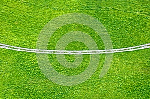 Unpaved countryside road across green field. Drone view from above