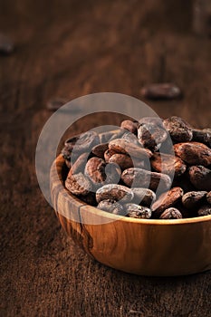 Unpeeled organic cocoa bean in bowl on wooden rustic table background. Copy space