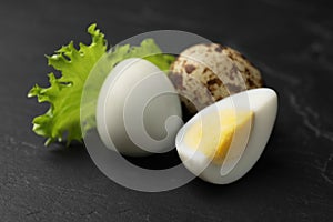 Unpeeled and peeled hard boiled quail eggs with lettuce leaf on black table, closeup