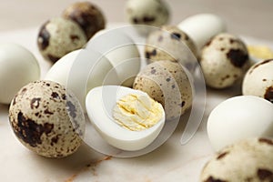 Unpeeled and peeled hard boiled quail eggs on light table, closeup