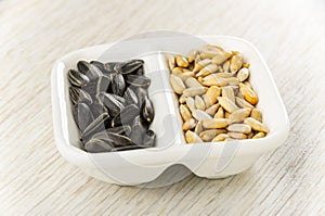 Unpeeled and peeled sunflower seeds in partitioned bowl on wooden table