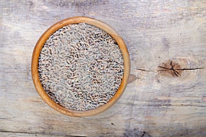 Unpeeled raw oats in a wooden plate on a wooden table