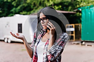 Unpleased elegant woman in trendy glasses talking on phone in morning. Outdoor shot of attractive g