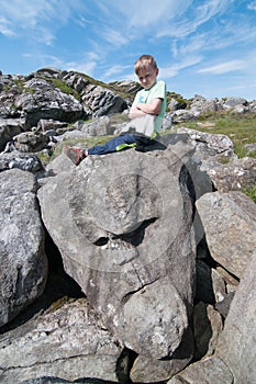 The unpleased kid sitting on the stone in the shape of face