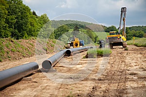 Unplugged gas pipeline in the coutryside diagonally from the left diagonally by photo with gas laying machines in the background