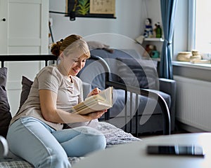 Unplugged smiling female reading book on sofa. Gadget free weekend. Concept of digital detox