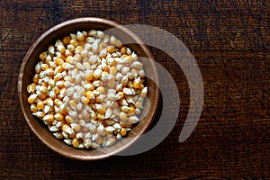 Unpopped popcorn in dark wooden bowl isolated on dark brown wood