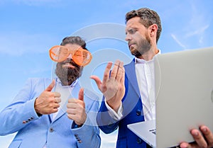 Unprofessional behaviour. Businessman with laptop serious while business partner ridiculous glasses looks funny. How