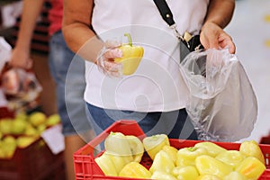 Unrecognisable adult woman chooses yellow pepers buys vegetables in a grocery store or supermarket, holds bio carrier