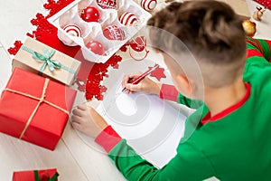 Unrecognisable boy wearing christmas pajamas writing letter to Santa on livingroom floor. Boy writing his christmas wishlist.