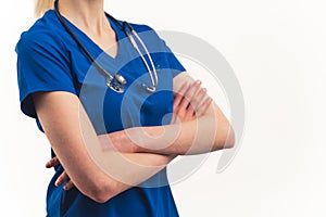 Unrecognisable female doctor in scrubs with stethoscope around neck standing confidently arms crossed close-up on torso